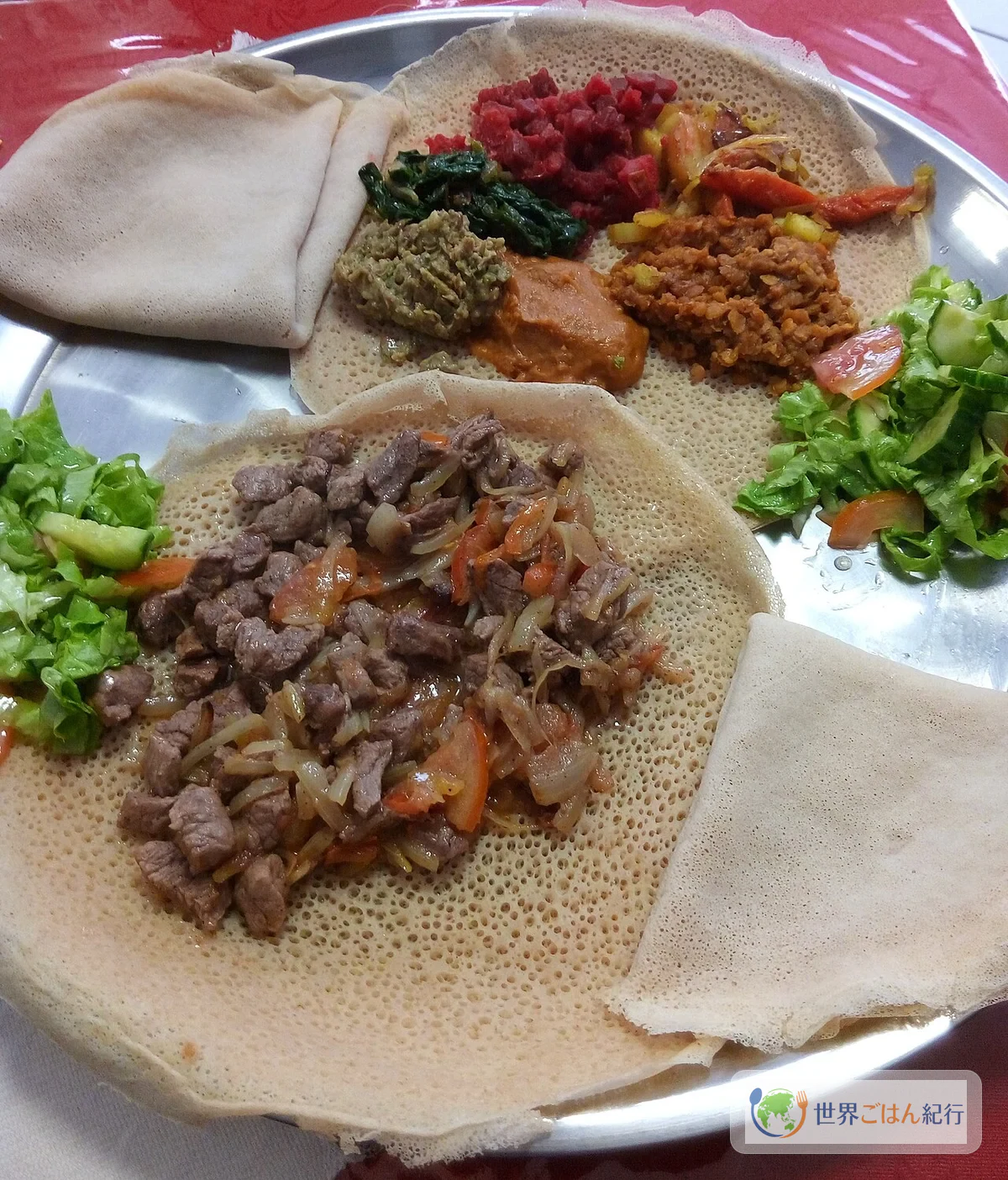 インジェラの上にミンチェットアビッシュ(ひき肉シチュー)と野菜のワットが盛られた一皿