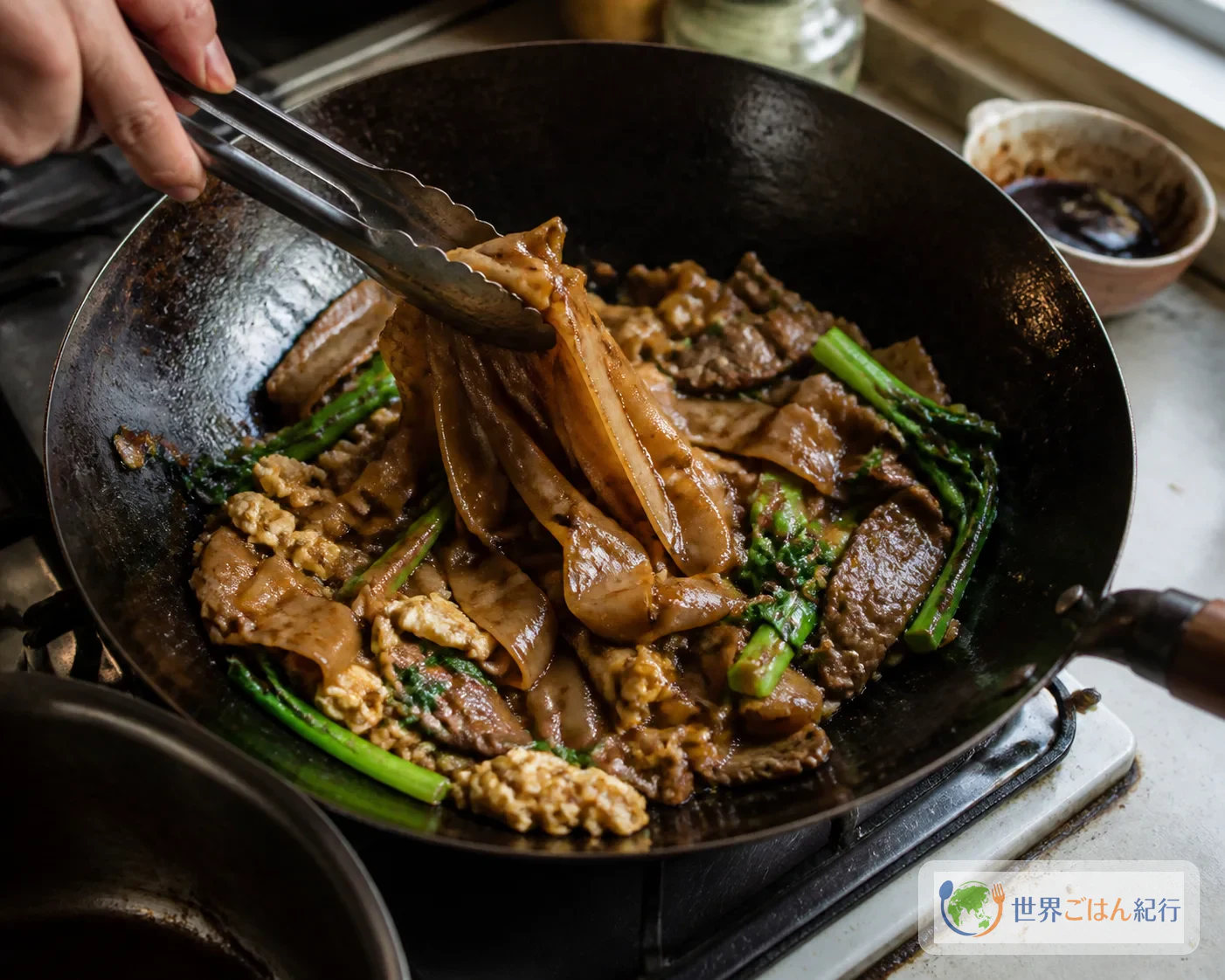 幅広の米麺へソースを回しかけ、カイランと牛肉を合わせている途中